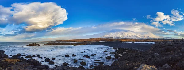 大西洋の冬の嵐の波に洗われたアイスランドの玄武岩の海岸 そして背景には珍しい雲の形と穏やかな朝の光に照らされた美しい雪に覆われた山々 — ストック写真