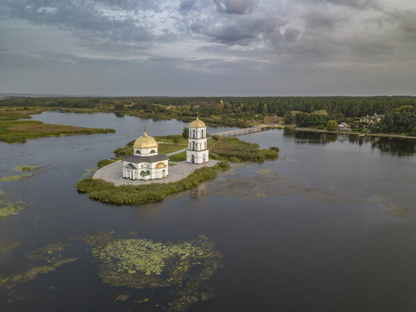 The gentle light of the rising sun illuminates the famous flooded church in Gusintsy and creates beautiful reflections on the water, Rzhishchev, Ukraine.