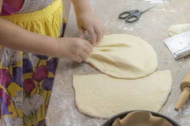 Mutfak tezgahında hamur şekillendiren eller. Ev yapımı hamur işi ya da turta kabuğunun renkli bir önlükle hazırlanması geleneksel yemek ve ev konforunu sembolize ediyor..