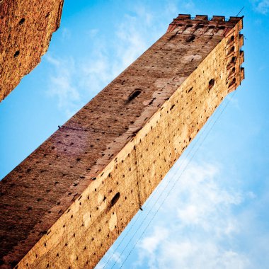 Uzun, dar bir ortaçağ taş kulesinin ince bulutlu, berrak mavi bir gökyüzüne uzanan yüzeyinin alçak açılı görüntüsü. Bologna. İtalya