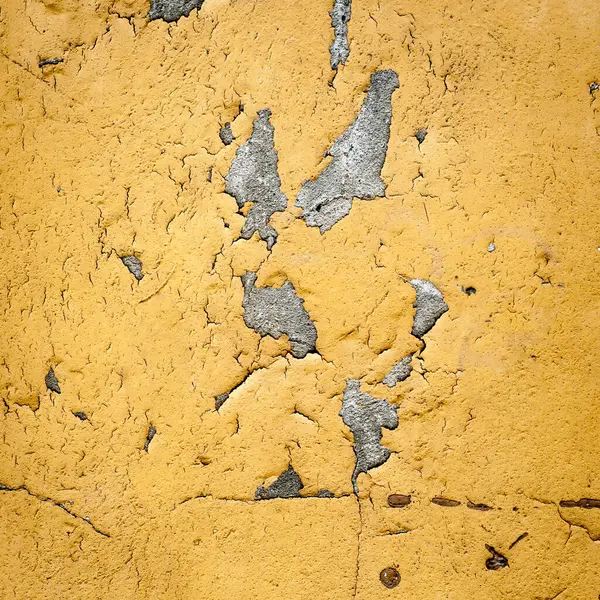 经过风吹日晒的黄色墙壁的特写 漆面有缺口 揭示了底层的纹理 裂缝和剥落层增加了这个老化表面的特征 由于多年的暴露 质感粗糙 理想的背景或纹理覆盖 免版税图库图片