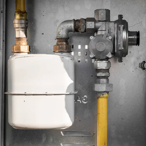 A close-up view of a gas meter and pipeline installation on a grey wall, featuring yellow pipes, metal fittings, and a white meter box.