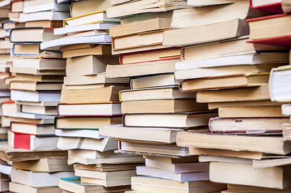 Üst üste dizilmiş kitapların dokulu kenarlarını görüntüleyerek, çeşitli renkleri ve koşullarını vurguluyor. Her kitap, eşsiz yıpranma ve yıpranma ile, farklı bir bilgi yolculuğunu temsil eder..