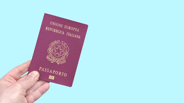 Italian biometric passport of the European Union held by hand isolated on a light blue background