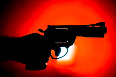 Siluet eli ve kırmızı arka planda bir silah..