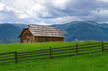 Tepedeki eski bir ahşap kulübe, dağların arka planına karşı. Kırsal alan