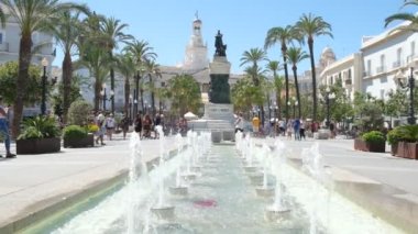 Cadiz, İspanya. 4 Eylül 2022. San Juan De Dios Meydanı 'ndaki fıskiyelerin yavaş çekim manzarası. Arka plandaki Segismundo Moret anıtının yanından geçen bir turist ve belediye binası..