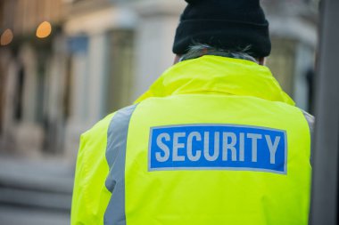 Londra, İngiltere. 28 Aralık 2017. Güvenlik görevlisi kameraya bakmıyor, parlak renkli bir ceket giyiyor. Arkasında güvenlik var. Londra, İngiltere 'de bir sokakta..