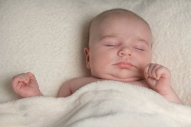 Sırtüstü uyuyan yeni doğmuş bir kızın portresi, krem bir battaniyeyle kaplanmış..