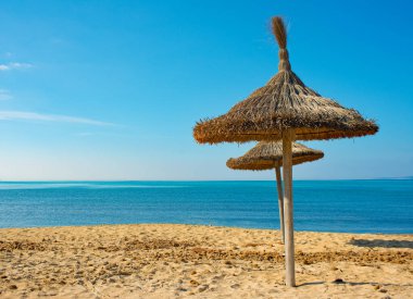 Akdeniz 'e bakan açık mavi gökyüzü ve insansız kumlu bir sahilde iki ahşap sazdan güneş gözlüğü..