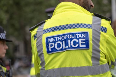 Londra, İngiltere. 19 Temmuz 2023. Londra 'nın merkezinde düzenlenen bir sokak gösterisine eşlik eden ve izleyen polis memurlarının giydiği yüksek görüşlü bir ceketin arkasında Metropolitan Polisi imzası var..
