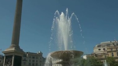 Trafalgar Meydanı, Londra, İngiltere. 14 Mayıs 2022. İnsanlarla dolu güneşli bir yaz gününde Londra, Trafalgar Meydanı 'ndaki çeşmelerin ve Nelson' s Column 'un sakin, yavaş çekim manzarası..