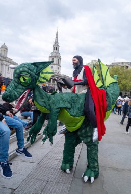 Londra, Birleşik Krallık. 21 Nisan 2024. Aziz George gibi giyinmiş ve yeşil bir ejderhaya binen sanatçı, Londra, İngiltere 'deki Trafalgar Meydanı' ndaki Aziz George Günü kutlamasında ziyaretçilerle buluşup selamlaşıyor..