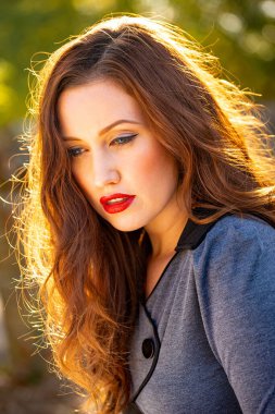 Güzel, dingin bir genç kadının portresi, uzun kahverengi saçları öğleden sonra güneşiyle aydınlanıyor.. 