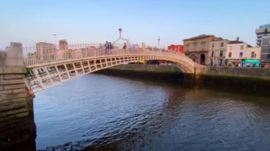 Dublin, İrlanda. 7 Eylül 2024. Akşamın ilerleyen saatlerinde, İrlanda 'nın Dublin şehrinden geçen Liffey Nehri üzerindeki tarihi Ha' Penny Köprüsü 'nü geçen insanların günbatımına şahit oluyoruz..