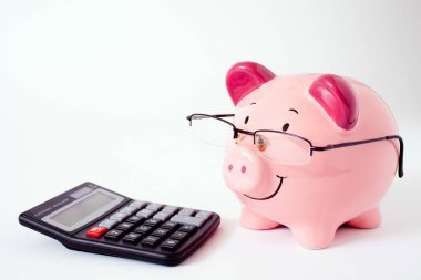 Smiling pink piggy bank wearing reading glasses and stood next to a calculator, against a plain white background with space for text. clipart