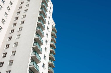 Açık mavi gökyüzüne karşı yüksek katlı bir apartman bloğunun alçak açılı görüntüsü.