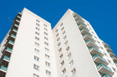 Açık mavi gökyüzüne karşı yüksek katlı bir apartman bloğunun alçak açılı görüntüsü.