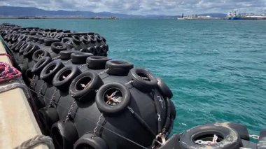 Cebelitarık 'taki rıhtım ekipmanlarının geniş açılı görüntüsü. Havada süzülen lastik çamurluklar güçlü rüzgar ve dalgalarla hareket ettirilir. Körfezin üstünde beyaz bulutlu mavi bir gökyüzü var..