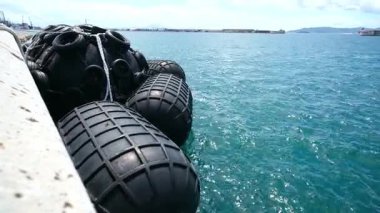 Cebelitarık 'taki rıhtım ekipmanlarının geniş açılı görüntüsü. Havada süzülen lastik çamurluklar güçlü rüzgar ve dalgalarla hareket ettirilir. Körfezin üstünde beyaz bulutlu mavi bir gökyüzü var..