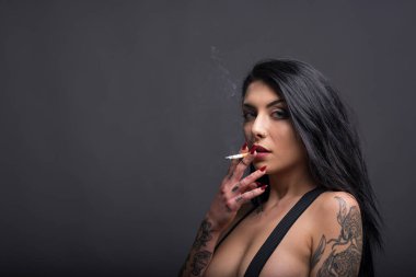 Siyah arka planda sigara içen dövmeli güzel bir kadının şehvetli portresi.