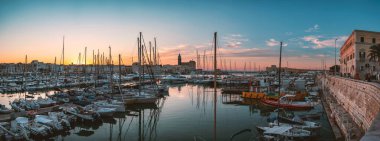 TRANI, İtalya - 2020 Trani limanı ve marinasının gün batımında iskeleye yanaşmış balıkçı tekneleri ve yatlarıyla panoramik manzarası.