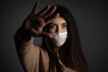 Korunmak için yüz maskesi takan genç bir kadın el hareketlerini durduruyor. Stüdyo resmi.