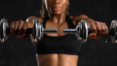 Sporty young black African woman portrait training with dumb-bells against black background.