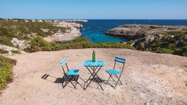 Masa ve sandalyeler Binidali koyuna bakan manzaralı bir yerde. Menorca, İspanya.