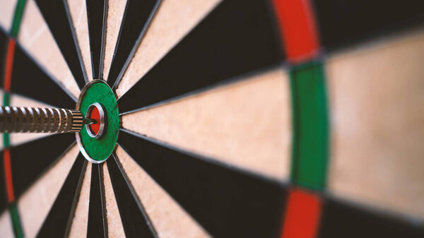 Dart arrow in the center of dartboard bulleye. Close up conceptual image of target and goal. Shallow depth of field.