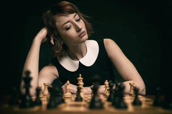 漂亮的红头发女人在深色背景下下下下棋 后期制作中添加的旧电影效果 — 图库照片
