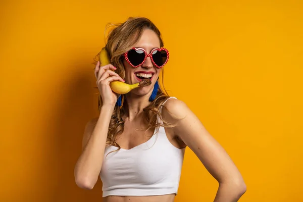 カラフルなオレンジの背景に対する電話をシミュレートバナナを保持した女性の肖像画 — ストック写真