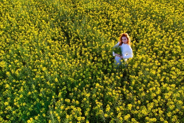 若い赤毛の女性は 黄色の菜の花畑で日没時に屋外で肖像画を描きます 空中風景 — ストック写真