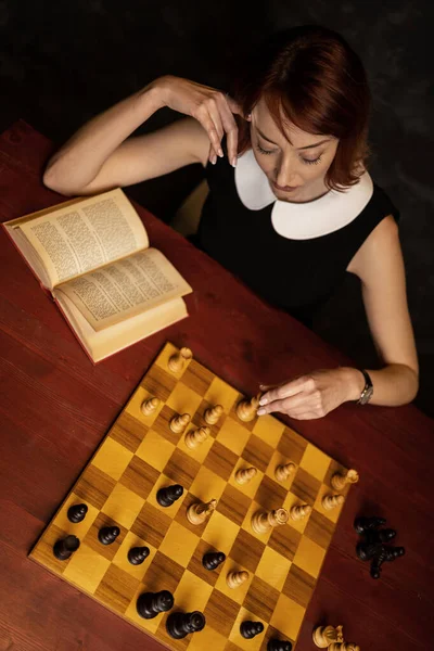 Жінка Вивчає Шахи Посібником Темному Тлі Тримаючи Королівську Фігуру Стокова Картинка