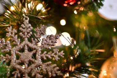 Çok güzel işlenmiş bir kar tanesi süsü Noel ağacında asılı. Şenlikli ışıklar ve mücevherlerle süslenmiş.