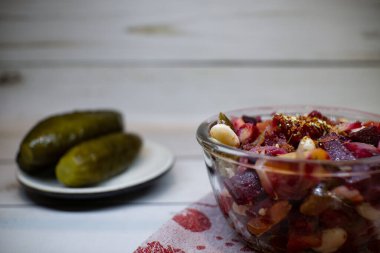 Vinaigrette in the glass bowl on the fabric napkin. Plate with pickles on the background.