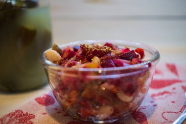 Vinaigrette with beans, dressed with seasonings. Jar of homemade pickles on the background