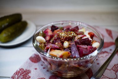 Vinaigrette in the glass bowl on the fabric napkin. Plate with pickles on the background.
