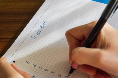 Ahşap masaüstüne yerleştirilmiş spiral deftere yazı yazan kadınların ellerini kapat. Yapılacaklar listesi