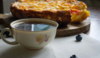 Antika porselen bardakta kahve. Arka planda şeftalili güveç turtası.