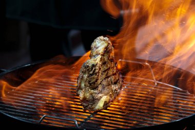 Izgara biftek baltası. Angus bifteği ateşte yanıyor. Ahşap kömür, kızarmış duman, açık hava restoranı. Sıcak barbekü yemeği, kemikleri yakın çekim