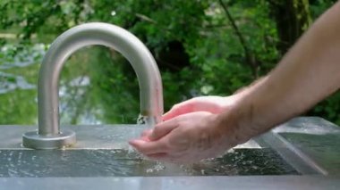 Yeşil arka planda duran musluğu olan bir adamın eli. Ellerinizi doğal olarak yıkayın. Ağır çekim video, tam HD. 
