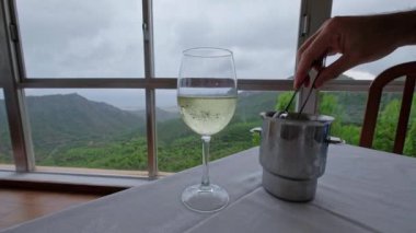 Restoranın masasındaki beyaz şaraba buz koyan bir adamın eli. Arka planda dağlar olan güzel bir manzara. Yavaş çekim videosu. 