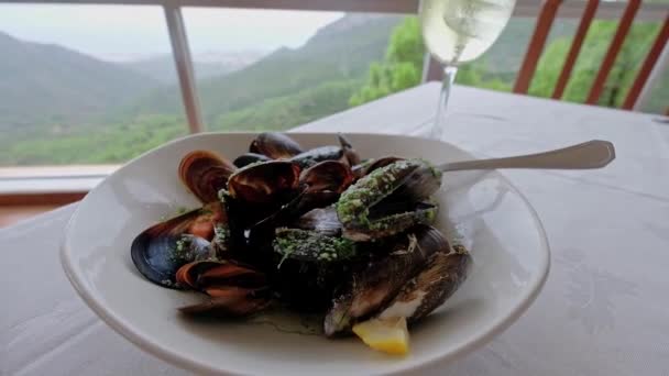 美しい白ワインのガラスとテーブルの上においしいムール貝 背景に山と美しい景色 スローモーションビデオ — ストック動画