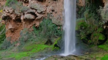 Gerçek zamanda güzel, büyük bir şelale. Kayalar, taşlar, yeşil ağaçlar ve çalılar. Yatay video. Turkuaz su rengi. 