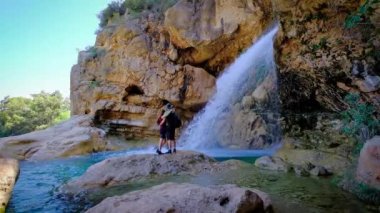 Çift ayakta ve sarılıyor. Ellerinizi kaldırın. Doğa yürüyüşü. Büyük, güzel bir şelale. Yavaş çekimde yatay video. Erkek ve kadın..