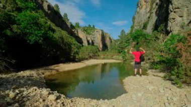 Bir adam vadideki bir gölün yanında geriniyor. Çocuk doğa yürüyüşü yapıyor. Yatay video.