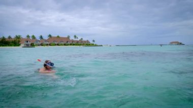 Kırmızı bikinili kadın şnorkelle yüzüyor ve el sallıyor. Maldivler 'de mutlu. Arka planda mavi turkuaz okyanus. Kız tropikal tatillerin tadını çıkarıyor. Yaz tatili konsepti. Yavaş çekim 4k video. 