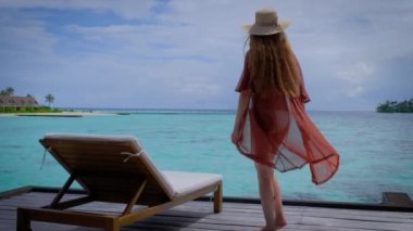 Bikinili kadın terasta. Kadın Maldivler 'de mutlu. Arka planda mavi turkuaz okyanus. Kız tropikal tatillerin tadını çıkarıyor. Yaz tatili konsepti. Yavaş çekim tam HD video. 