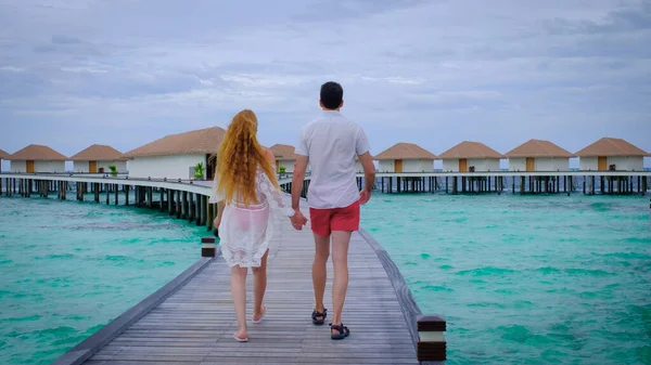 夫婦は歩いて手を握っている モルディブでは男性と女性が幸せです 背景に青いターコイズブルーの海 女の子は熱帯の休日を楽しんでいます 夏の旅行休暇のコンセプト — ストック写真